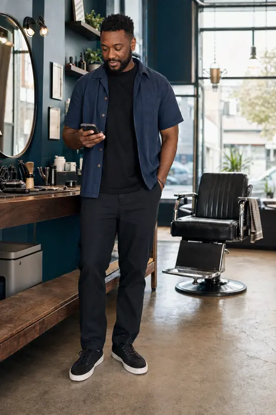 A self-employed barber checking his phone in his studio